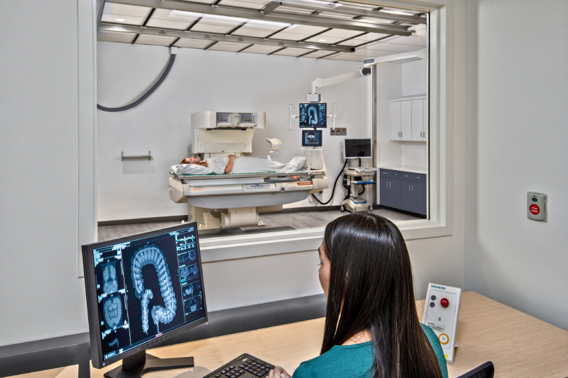 Medical imaging technician reviewing diagnostic images while patient undergoes exam