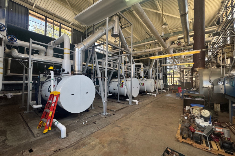 Industrial boiler room with large white pressure vessels and overhead piping system